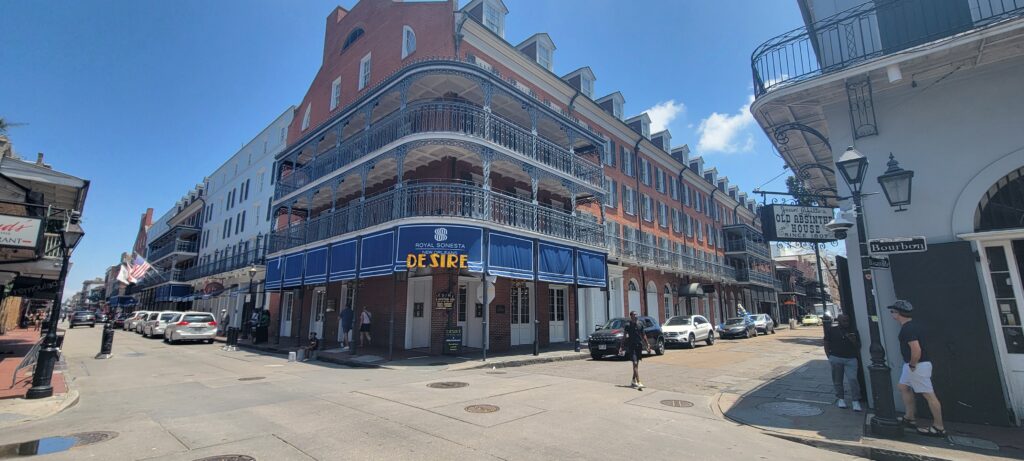 View of the iconic Royal Sonesta New Orleans Hotel on Bourbon Street, showcasing its classic Creole townhouse architecture with intricate ironwork balconies under a clear blue sky.