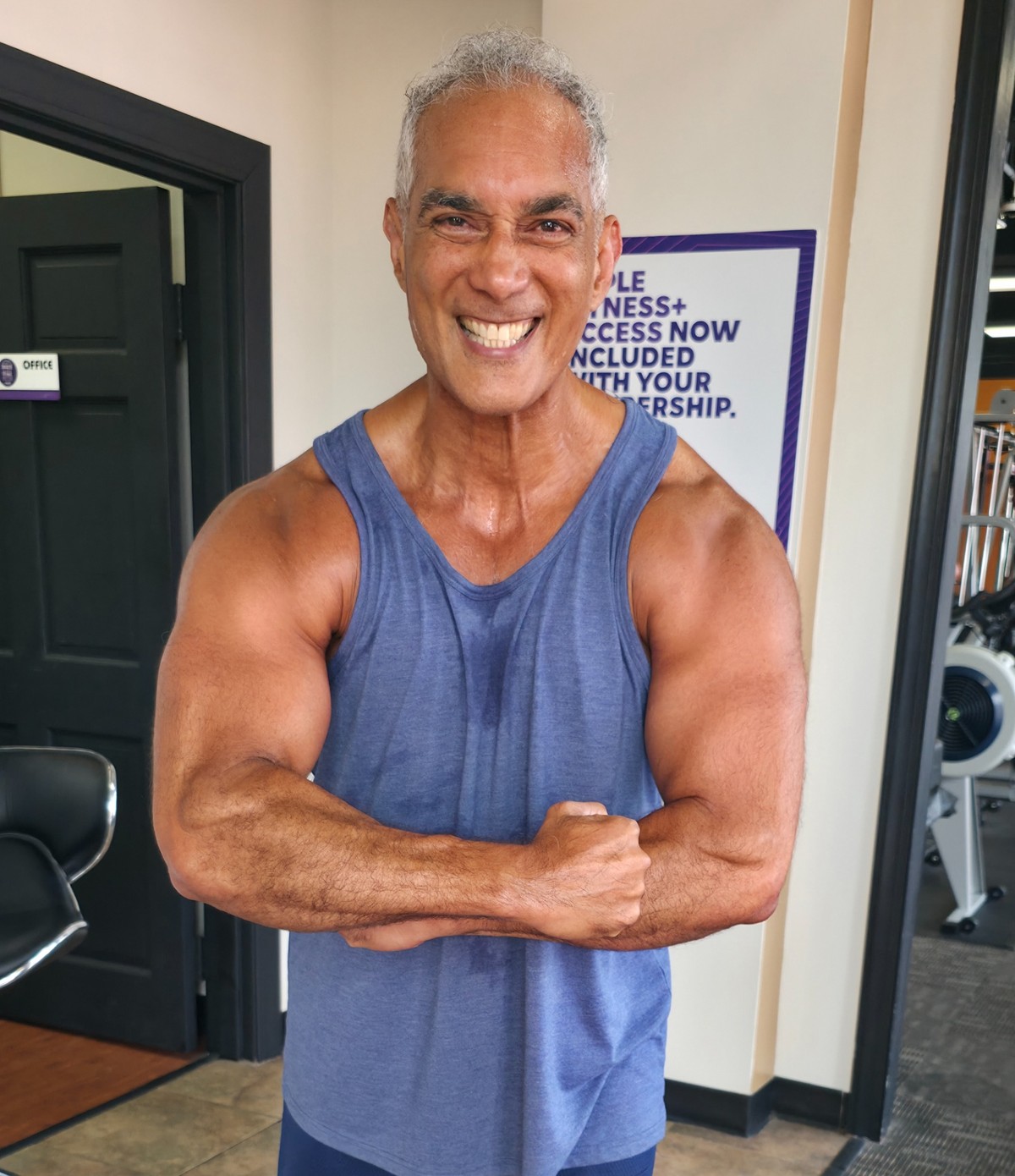 Curtis Matthews smiling at the gym after a workout, wearing a blue tank top and flexing his arms.